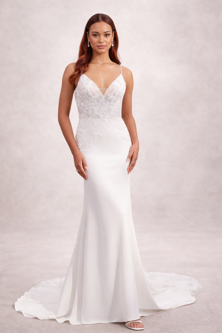 A woman in a fitted, white wedding dress with a lace bodice and thin straps, standing against a neutral background.