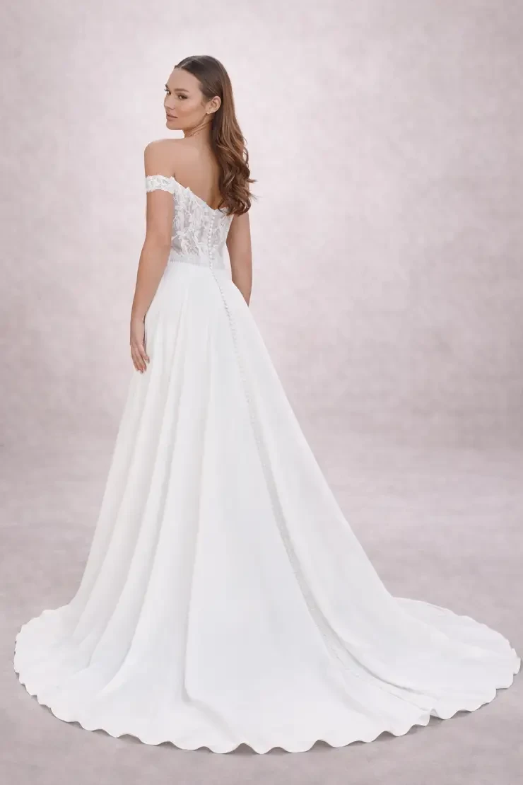 A woman wearing a white off-the-shoulder wedding gown with a fitted bodice and a full skirt.