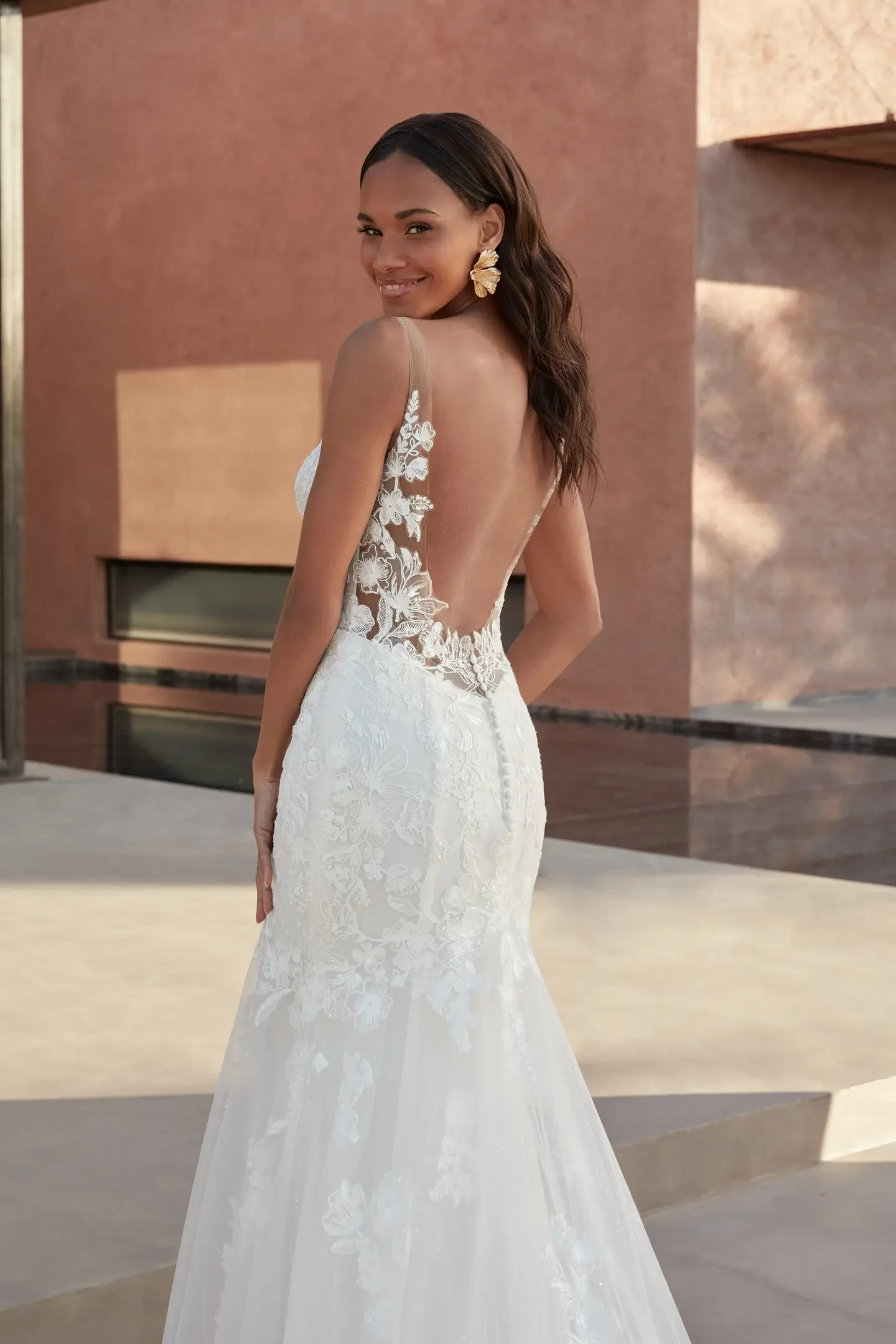 Model is wearing a sleek fit and flare wedding dress with a plunging Sabrine neckline and an open low back