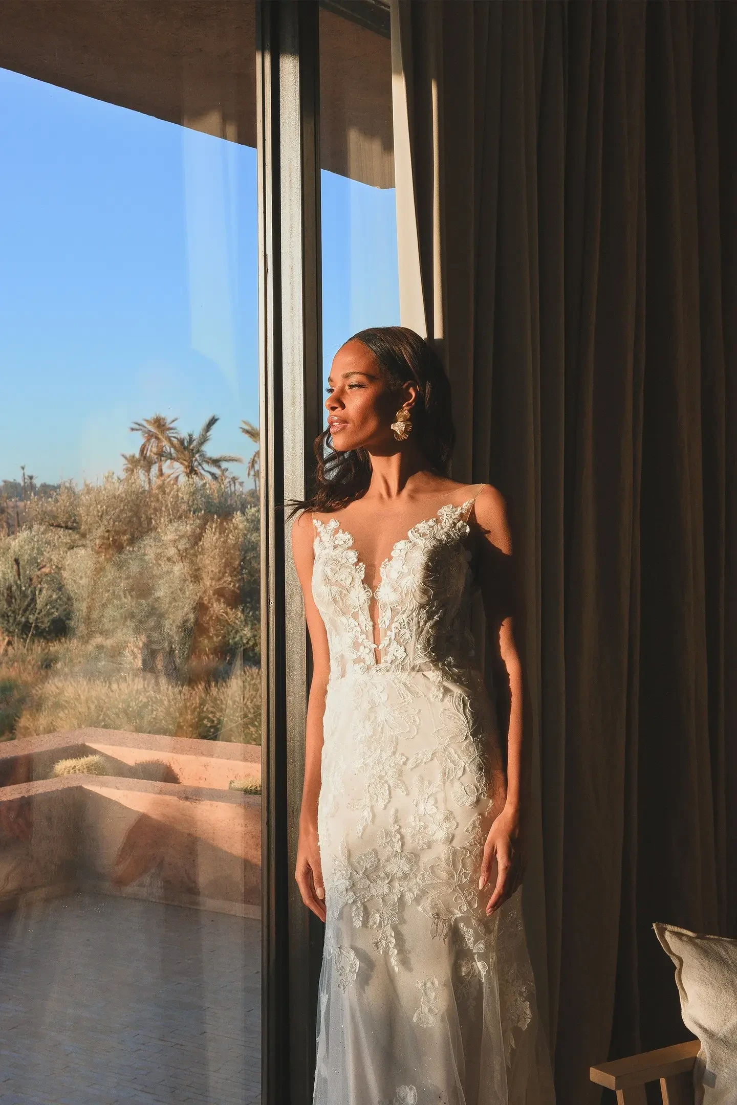 Model is wearing a sleek fit and flare wedding dress with a plunging Sabrine neckline and an open low back