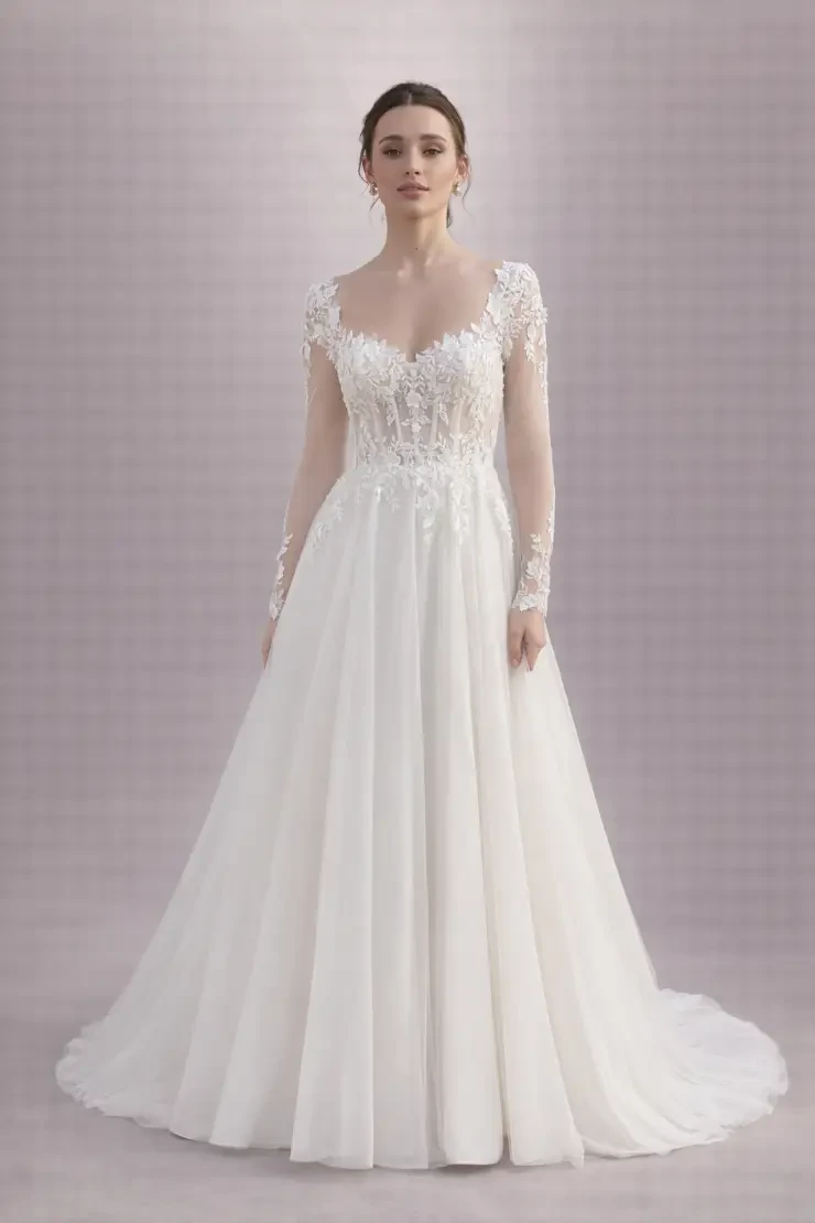A model wearing a white wedding dress with long sleeves, a fitted bodice adorned with embellishments, and a flowing skirt.
