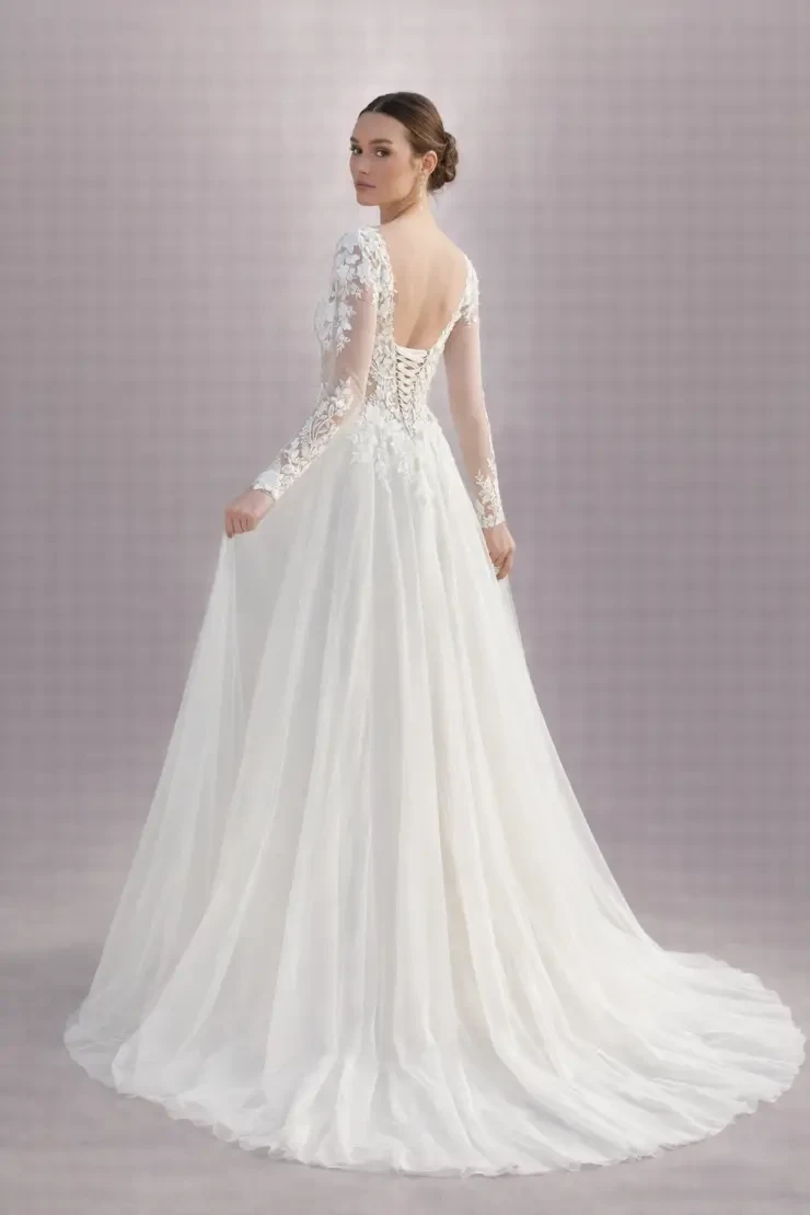 A model wearing a white wedding dress with long sleeves, a fitted bodice adorned with embellishments, and a flowing skirt.