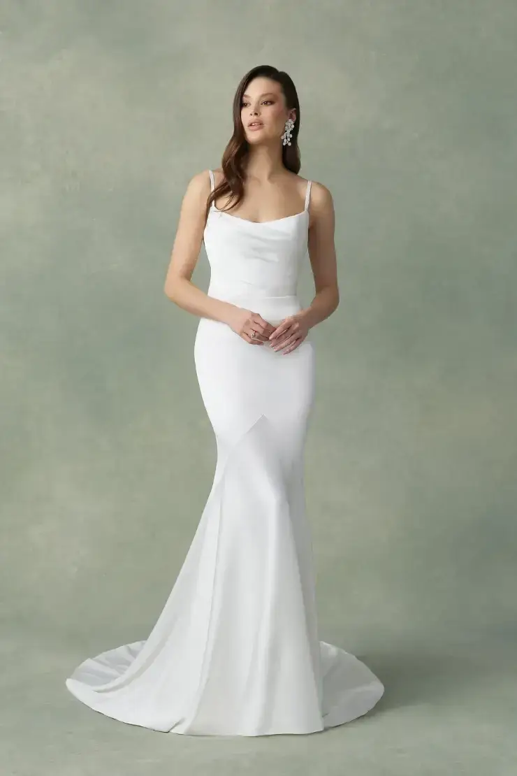 A woman poses in a fitted white gown with a mermaid silhouette and a simple, elegant design.