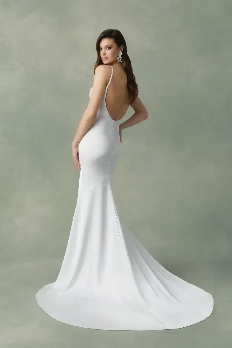 A woman in a white dress with a low back posing against a textured backdrop.