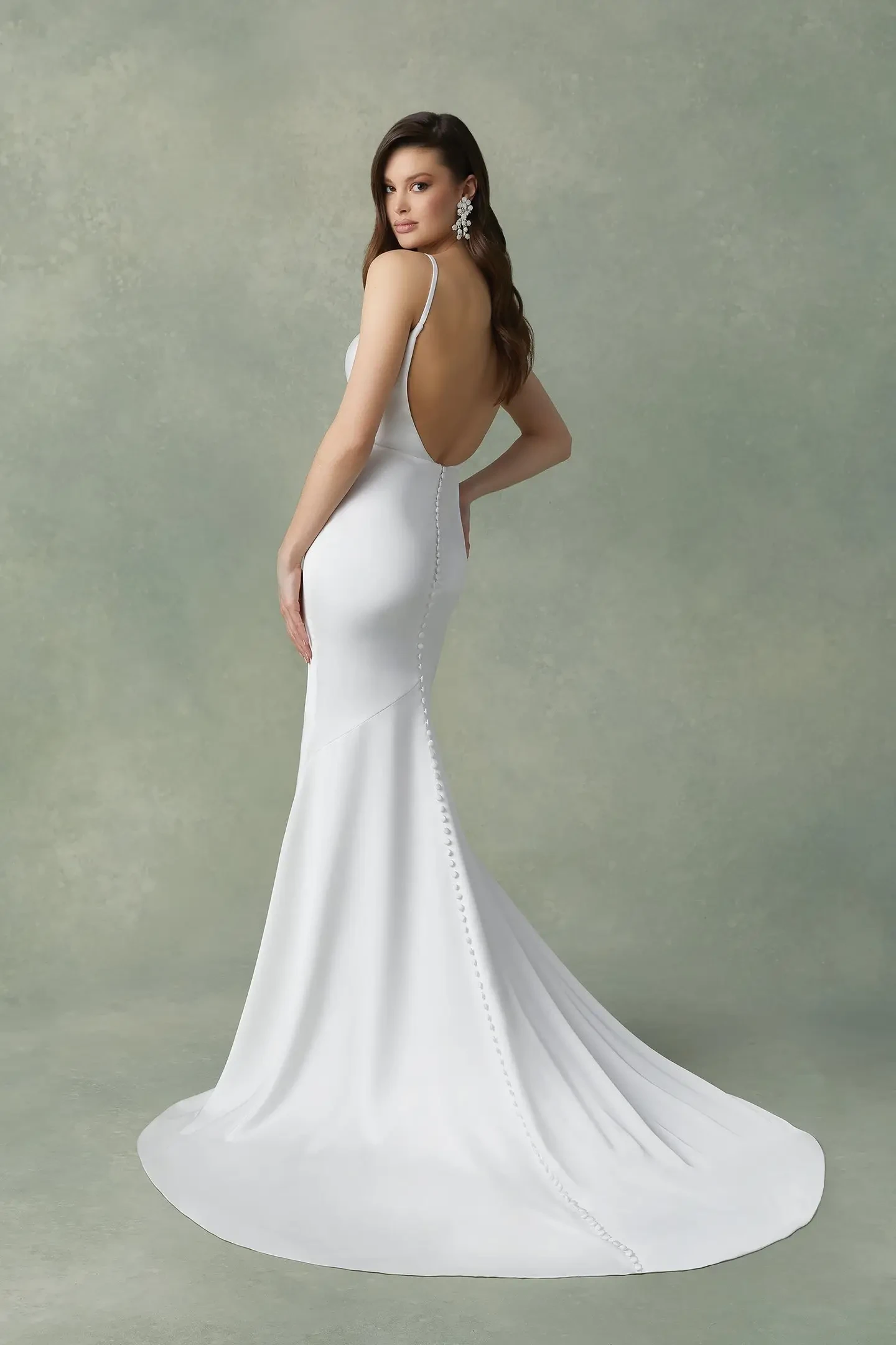 Model is wearing a charmeuse satin wedding dress with thin spaghetti straps, scoop neckline, low open back, and asymmetrical pleating.